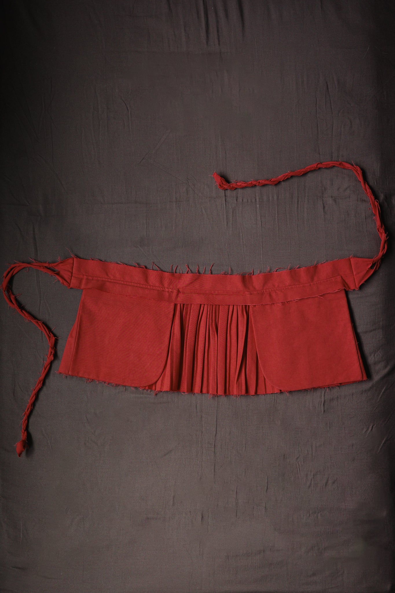 Red Goma apron with structured waistband and pleated construction.