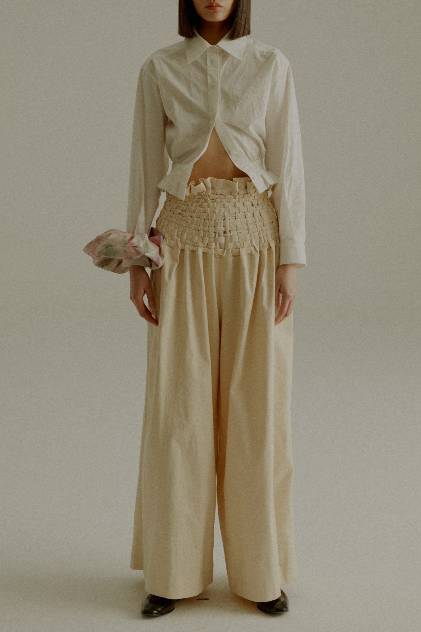 A model wearing the Rose Shirt, a cropped shirt made from 100% organic cotton with handwoven detailing at the waist. Styled with the Sisa Pants. The model is shown in front, side, and back views.