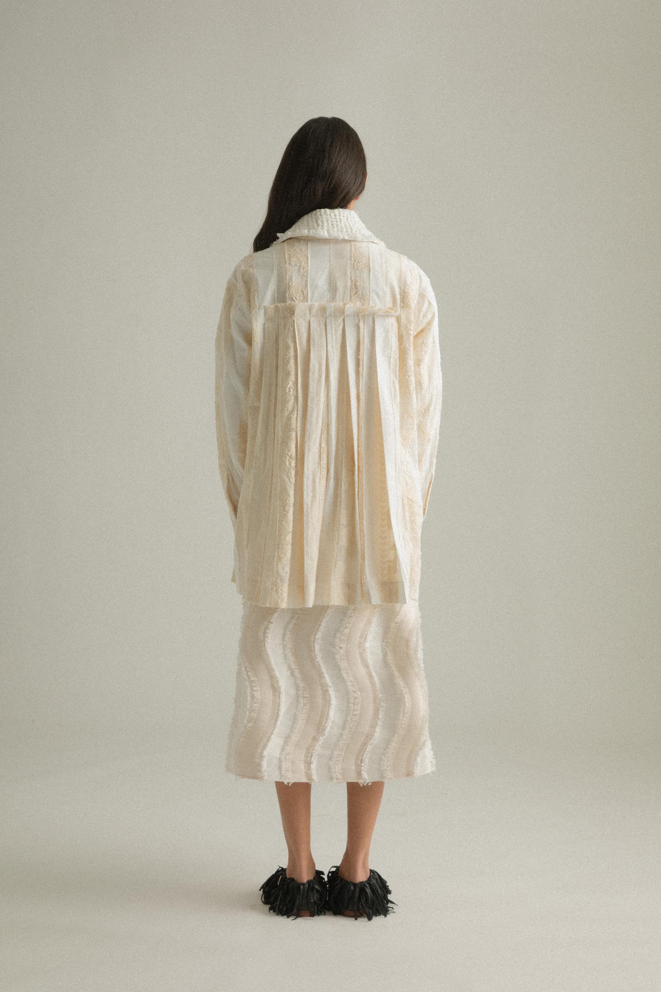 A model wearing the Bing Top, a blend of cotton, polyester, silk, and lyocell in natural tones. The top has a structured front with subtle pleating and a back-tied design, styled over the Lena Dress. The model is shown in front, side, and back views to showcase the top’s texture and fit