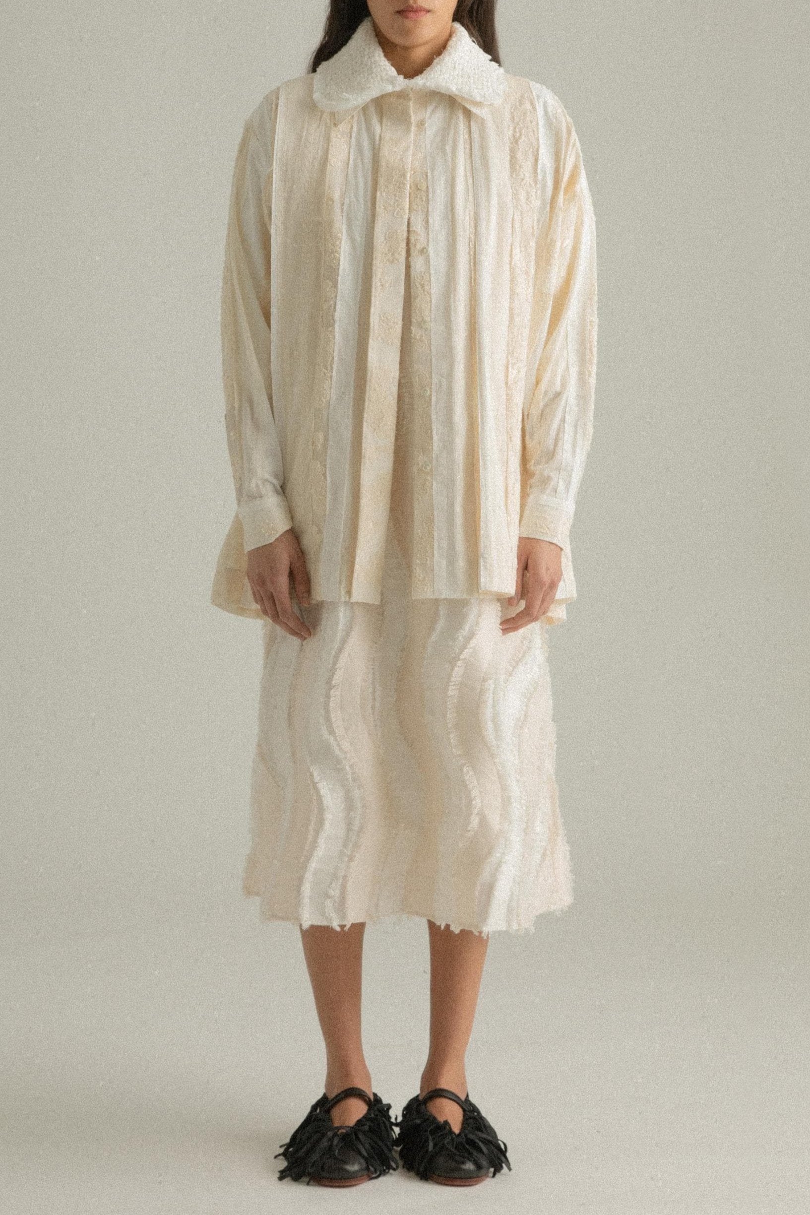 A model wearing the Bing Top, a blend of cotton, polyester, silk, and lyocell in natural tones. The top has a structured front with subtle pleating and a back-tied design, styled over the Lena Dress. The model is shown in front, side, and back views to showcase the top’s texture and fit