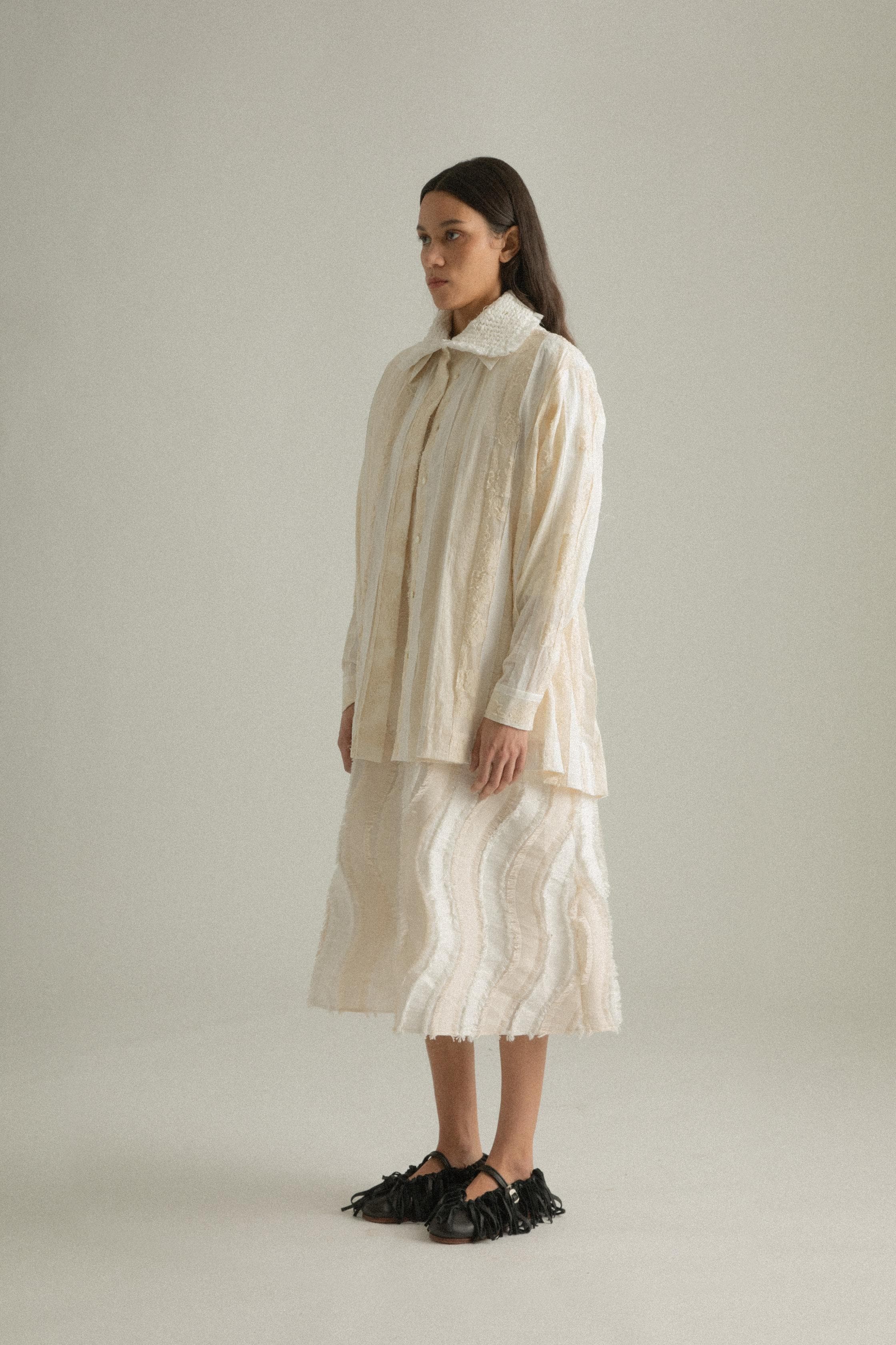 A model wearing the Bing Top, a blend of cotton, polyester, silk, and lyocell in natural tones. The top has a structured front with subtle pleating and a back-tied design, styled over the Lena Dress. The model is shown in front, side, and back views to showcase the top’s texture and fit