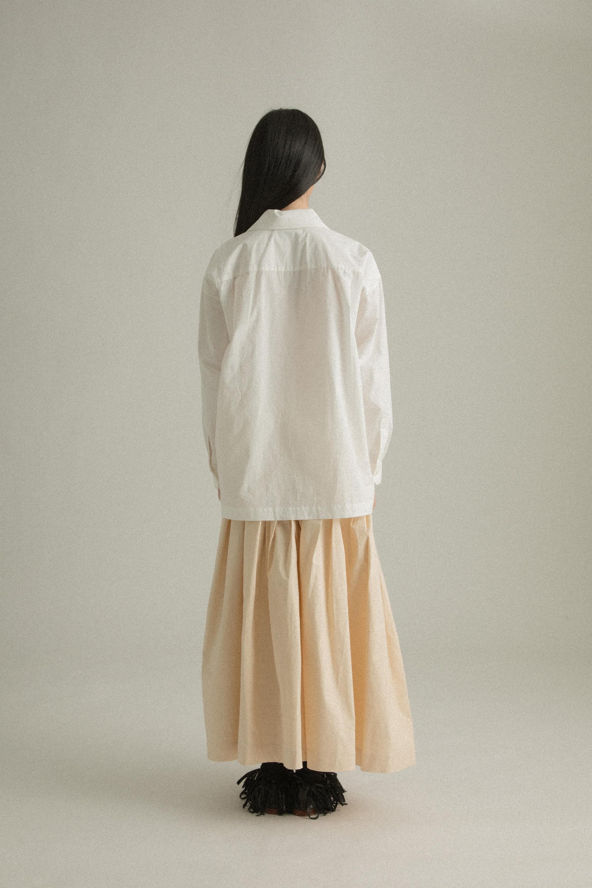 A model wearing the Charlotte Shirt, made from 100% organic cotton with intricate hand-knit detailing on the chest pocket. The shirt is paired with the Clara Skirt, presenting a balanced and fluid ensemble. The model is shown in front, side, and back views to showcase the shirt’s relaxed fit and unique design elements.