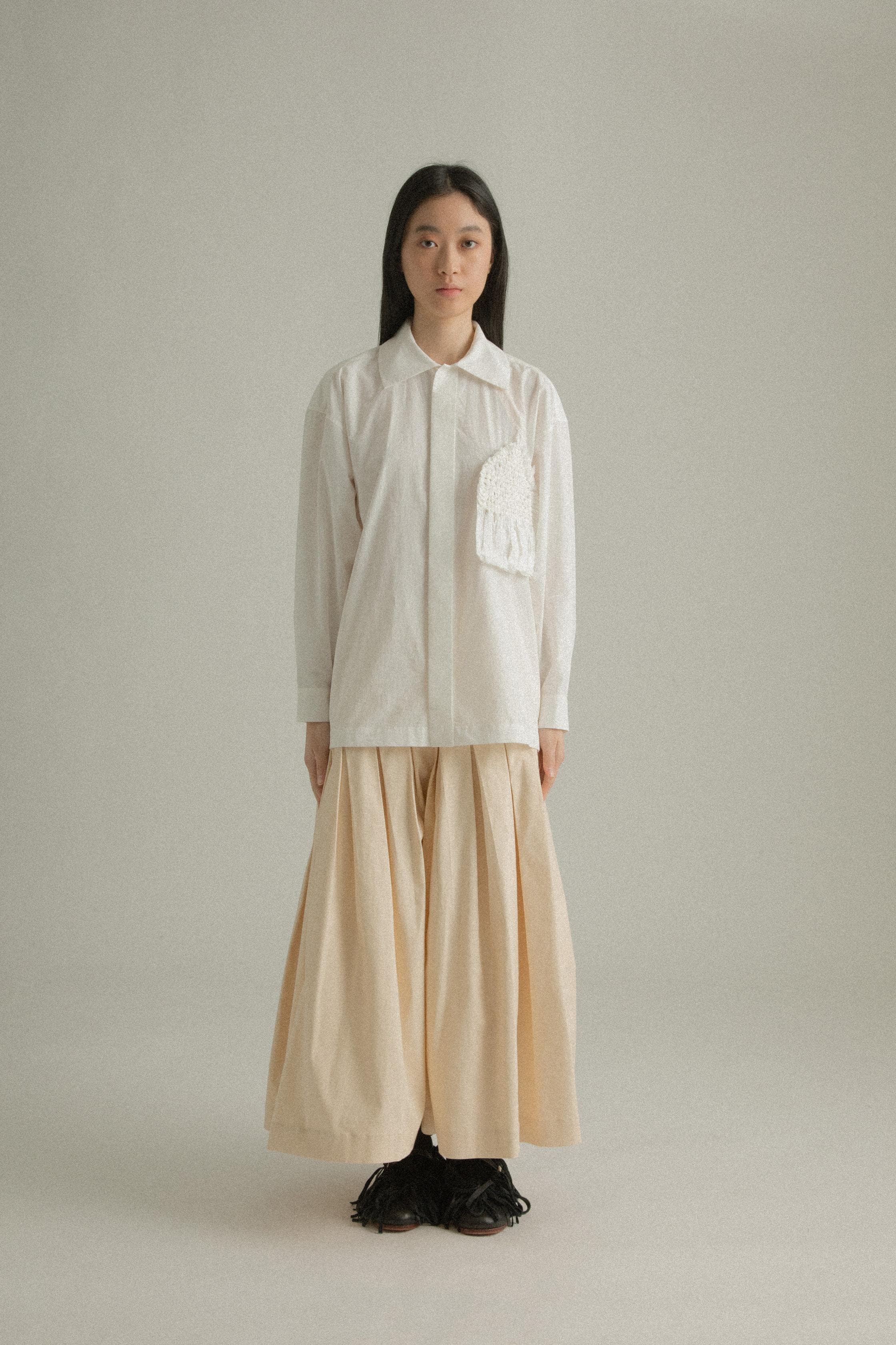 A model wearing the Charlotte Shirt, made from 100% organic cotton with intricate hand-knit detailing on the chest pocket. The shirt is paired with the Clara Skirt, presenting a balanced and fluid ensemble. The model is shown in front, side, and back views to showcase the shirt’s relaxed fit and unique design elements.