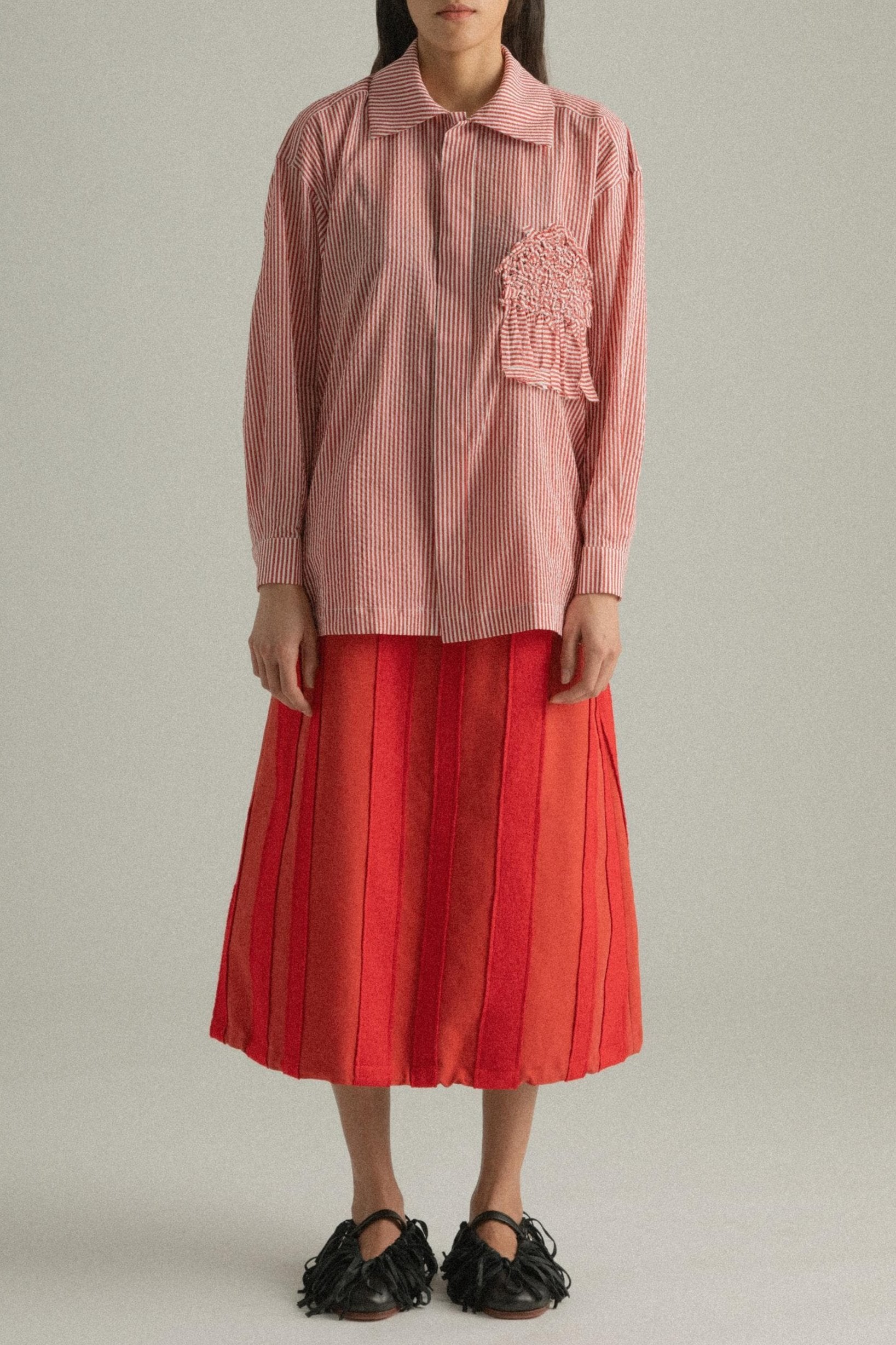 A model wearing the Charlotte Shirt, made from 100% organic cotton with woven stripes and a hand-knit detailed chest pocket. The shirt is styled with the Lulu Skirt, presenting a cohesive look. The model is shown in front, side, and back views to showcase the shirt’s relaxed fit and design elements