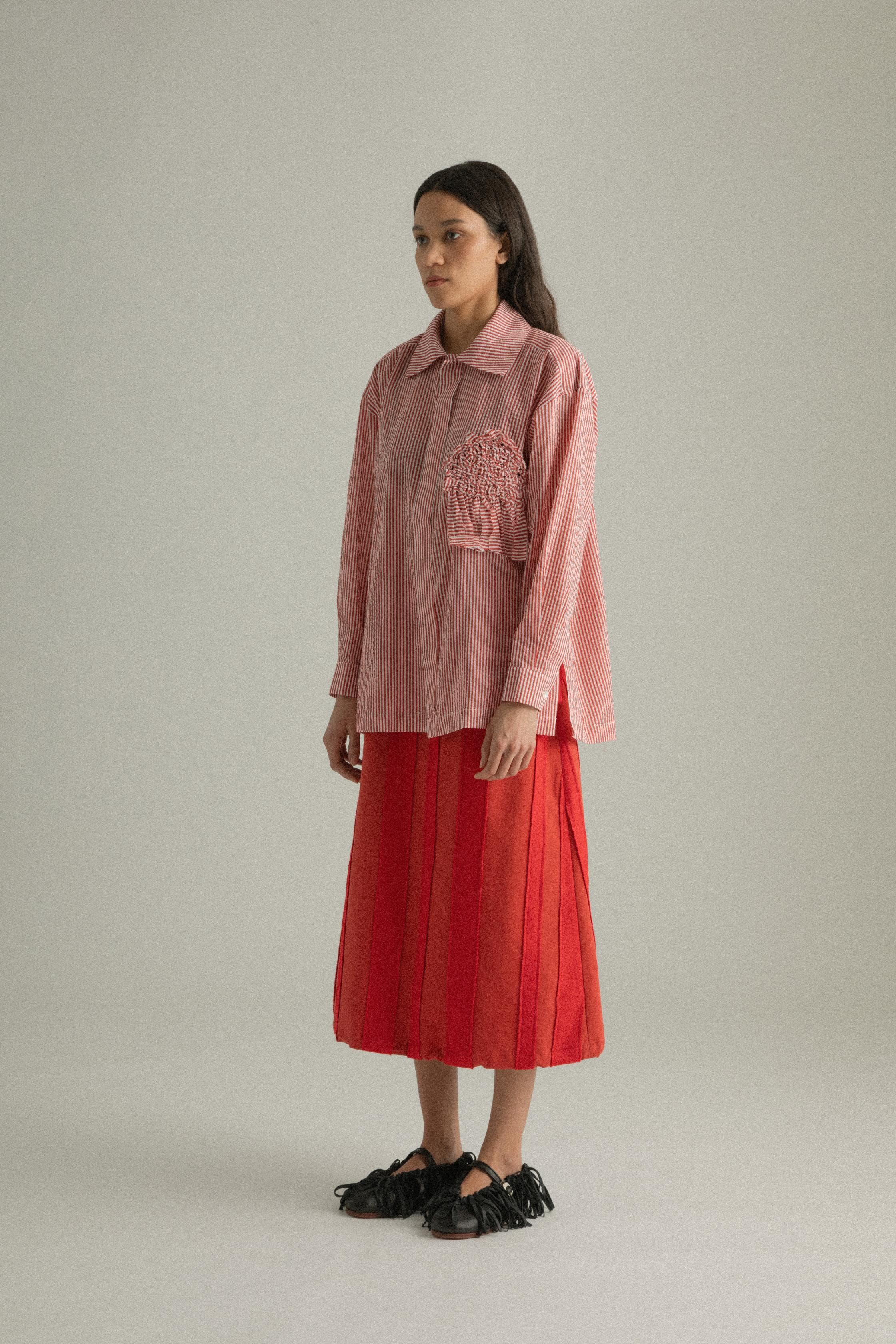 A model wearing the Charlotte Shirt, made from 100% organic cotton with woven stripes and a hand-knit detailed chest pocket. The shirt is styled with the Lulu Skirt, presenting a cohesive look. The model is shown in front, side, and back views to showcase the shirt’s relaxed fit and design elements.