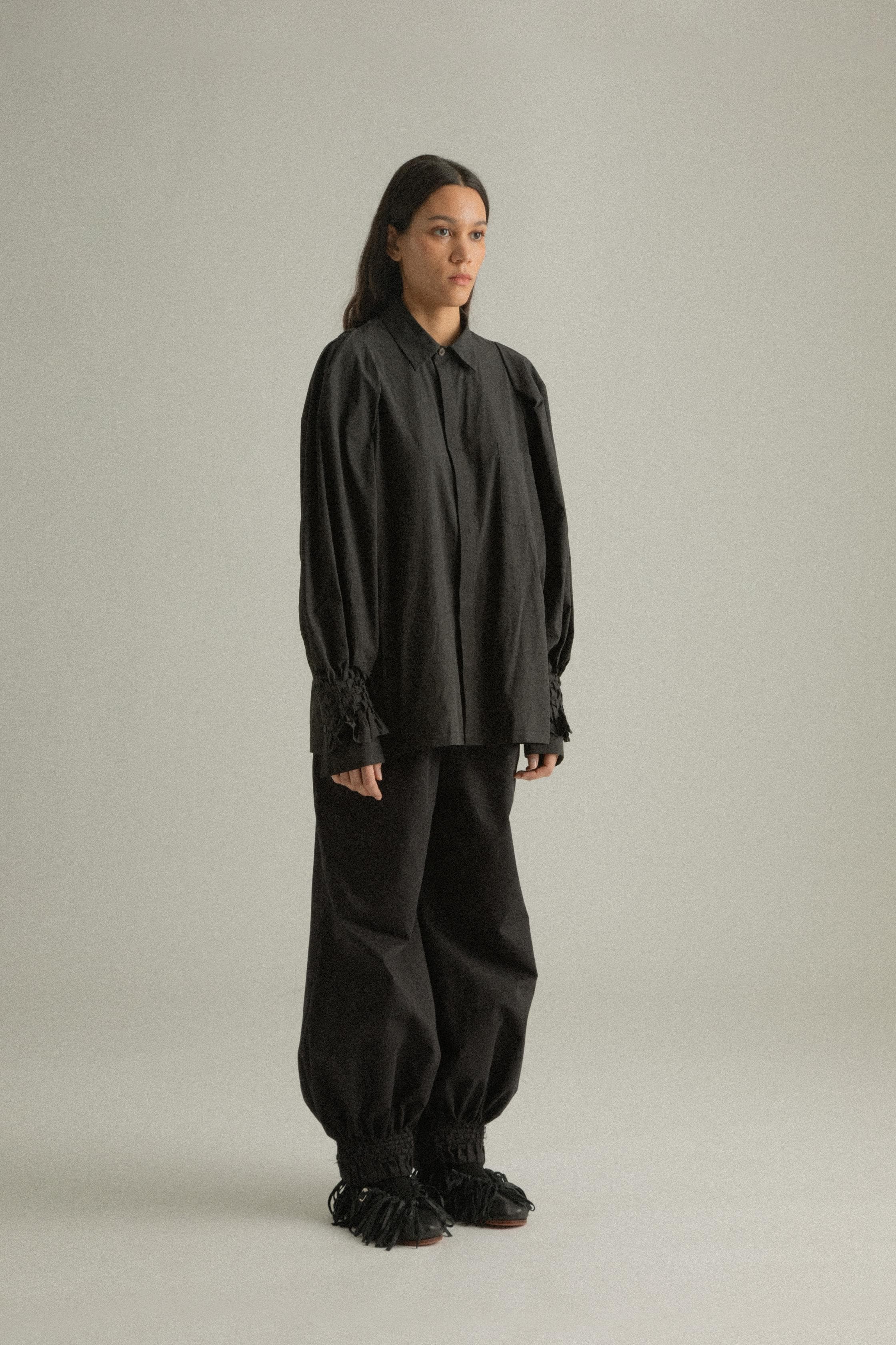 A model wearing the Elias Top, crafted from 100% organic cotton, featuring handwoven sleeves and intricate hand-knit cuffs. Paired with the Qira Pants for a cohesive look. The model is shown in front, side, and back views to highlight the top’s relaxed fit and natural texture.