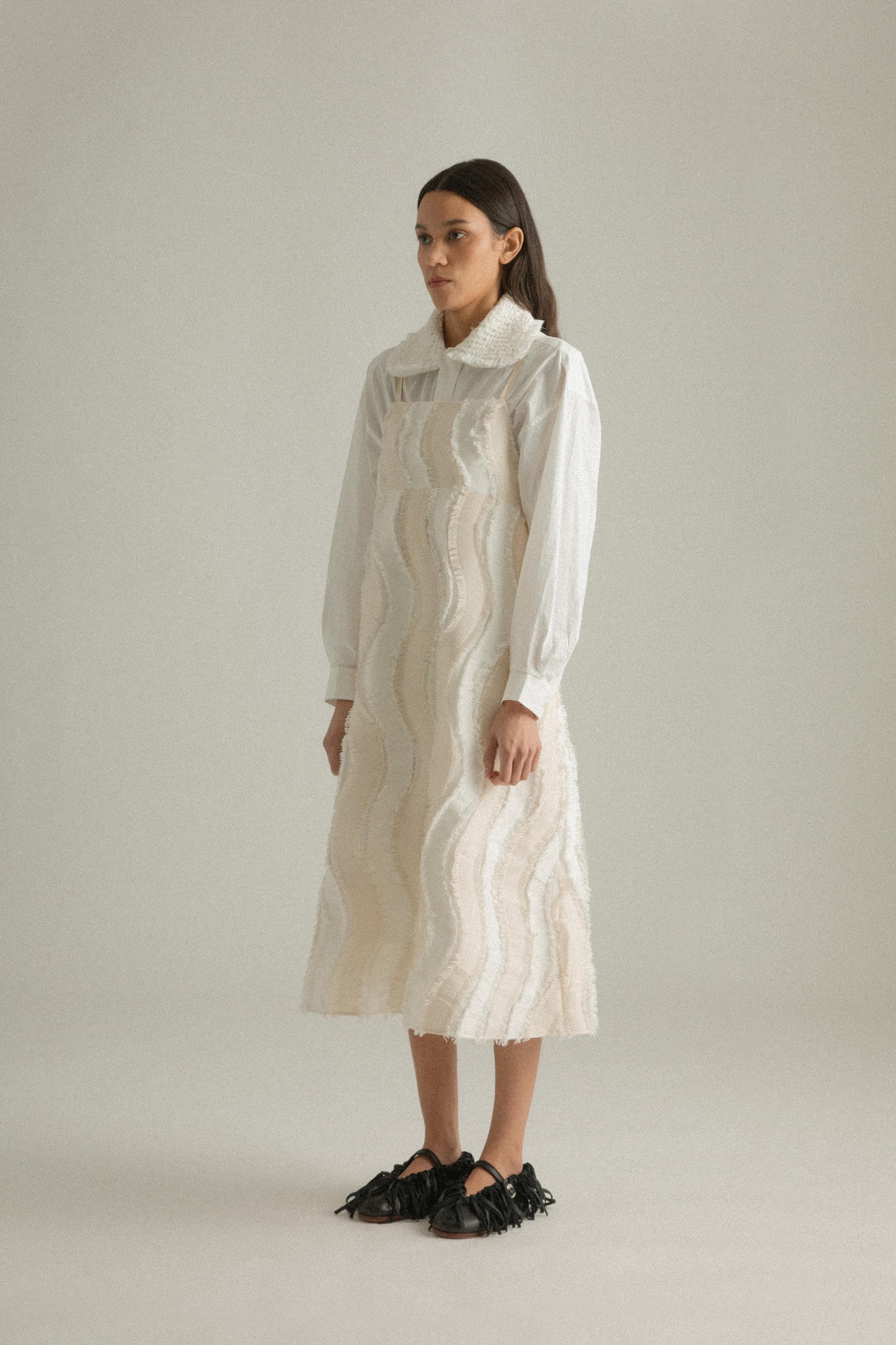 A model wearing the Lena Dress, featuring a wave-like patchwork design made from a blend of cotton, acrylic, and polyester. The model is shown in front, side, and back views to highlight the dress’s texture and A-line silhouette.