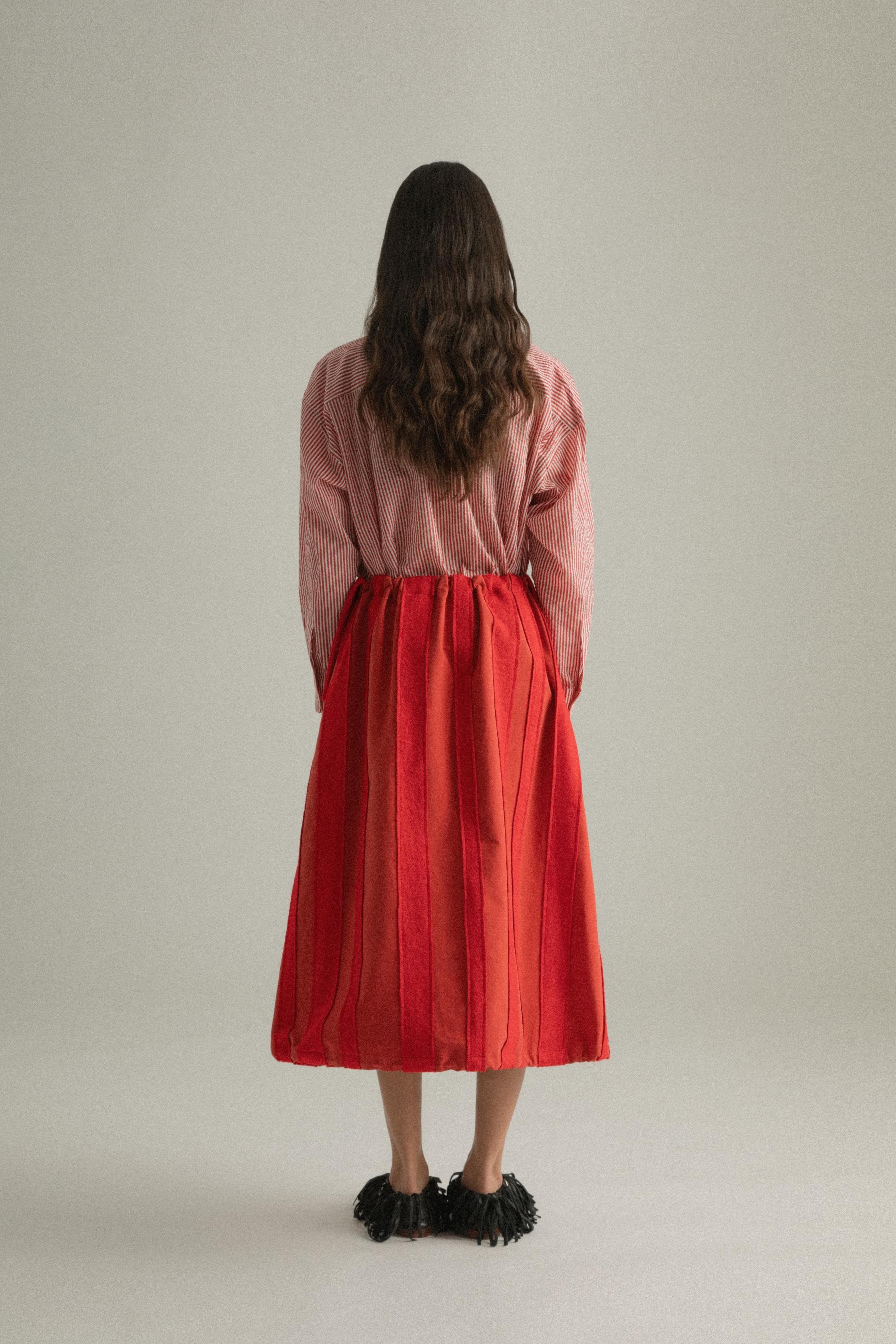 A model wearing the Lulu Skirt in a classic A-line silhouette, crafted from 100% bony cotton with a unique patchwork design. The skirt is styled with the Charlotte Shirt, presenting a layered and colorful look. The model is shown in front, side, and back views.