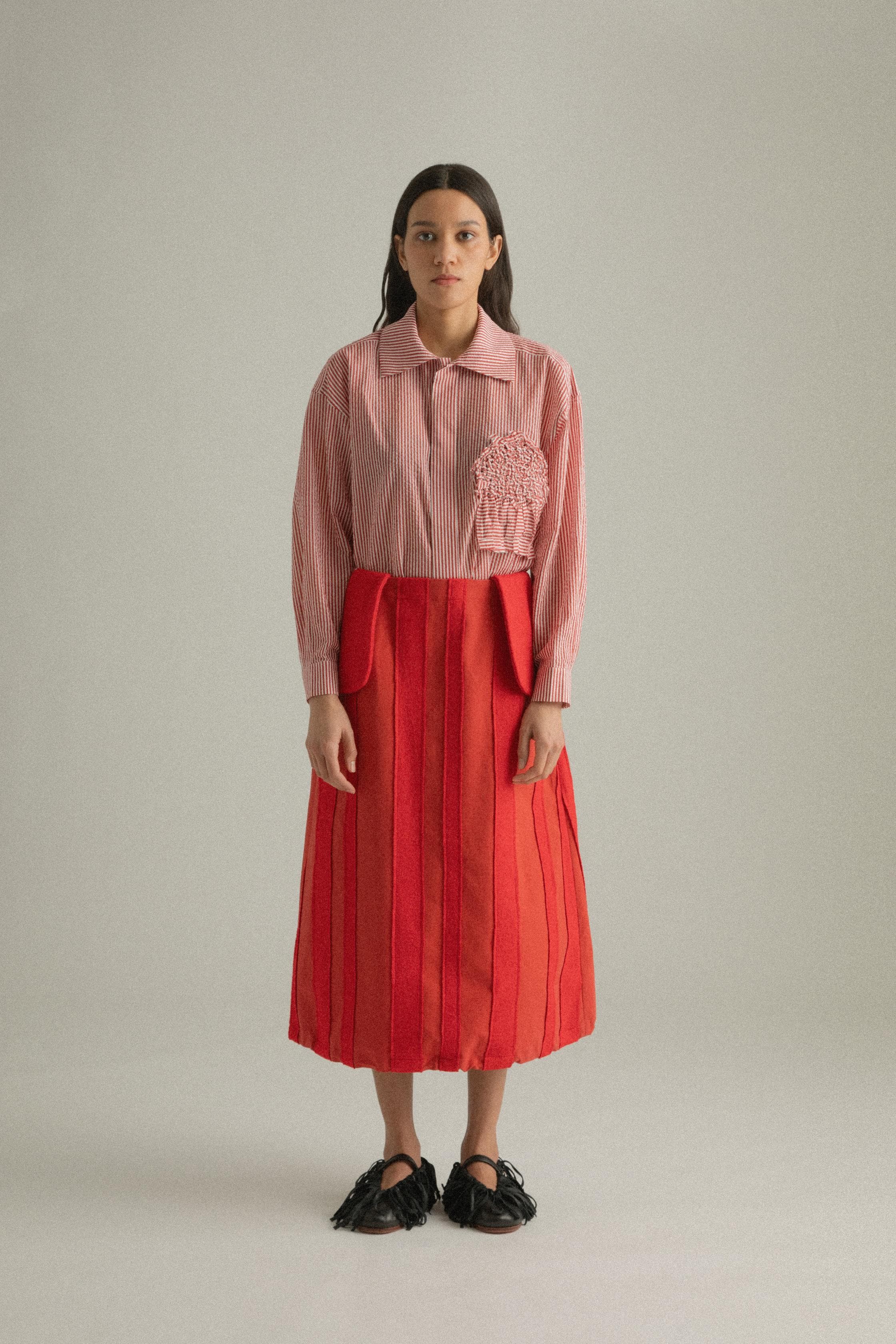 A model wearing the Lulu Skirt in a classic A-line silhouette, crafted from 100% bony cotton with a unique patchwork design. The skirt is styled with the Charlotte Shirt, presenting a layered and colorful look. The model is shown in front, side, and back views.
