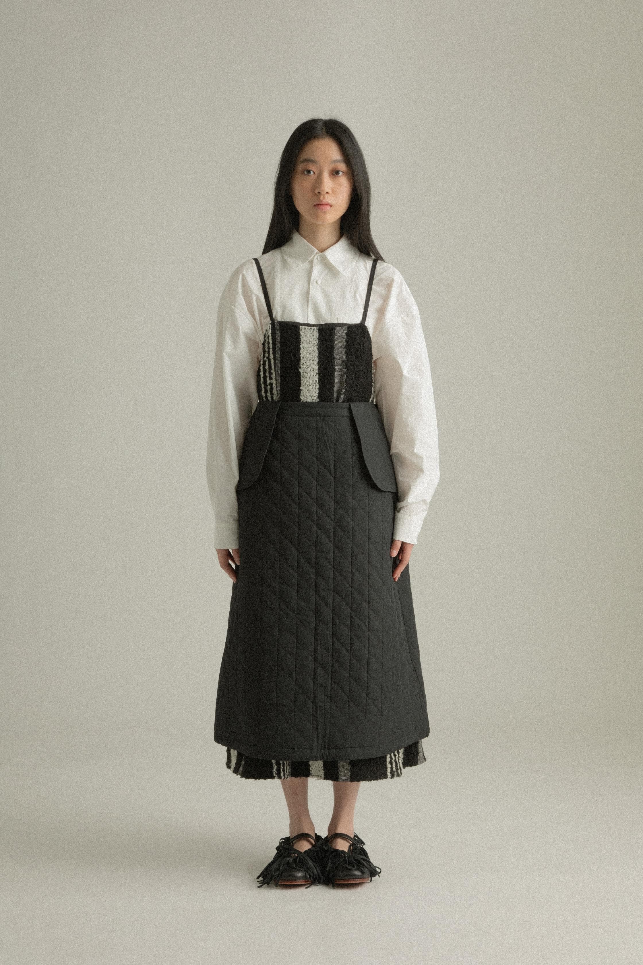 A model wearing the Lulu Skirt, crafted from 100% organic cotton with a quilted texture. The skirt features an A-line silhouette and is layered over the Lena Dress, adding dimension and warmth. The model is shown in front, side, and back views.