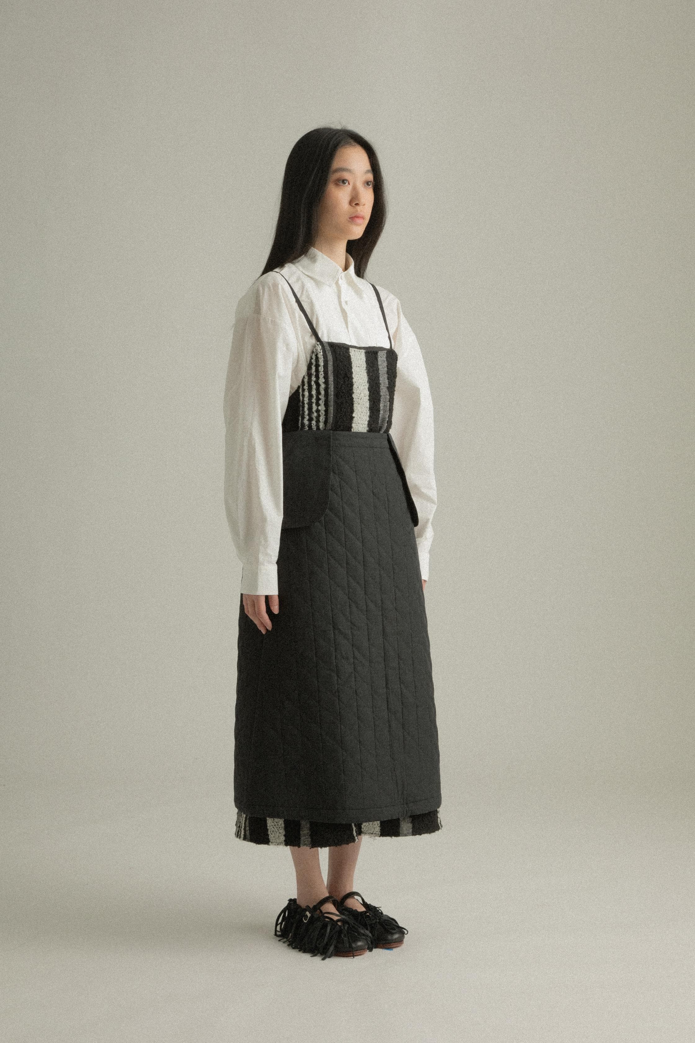 A model wearing the Lulu Skirt, crafted from 100% organic cotton with a quilted texture. The skirt features an A-line silhouette and is layered over the Lena Dress, adding dimension and warmth. The model is shown in front, side, and back views.