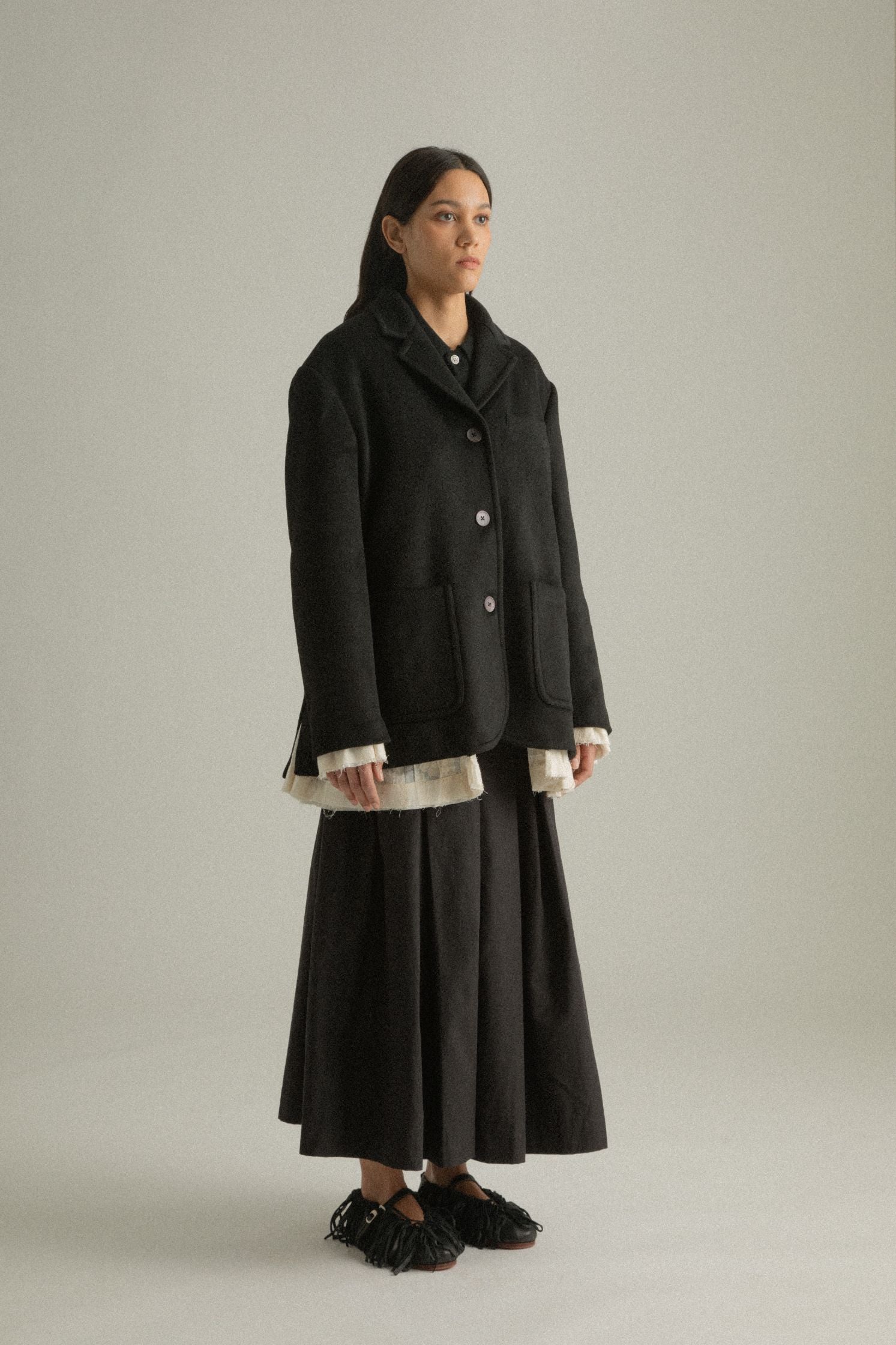 Side view of the Martha Coat’s black wool side, highlighting its structured silhouette and flowing lines.