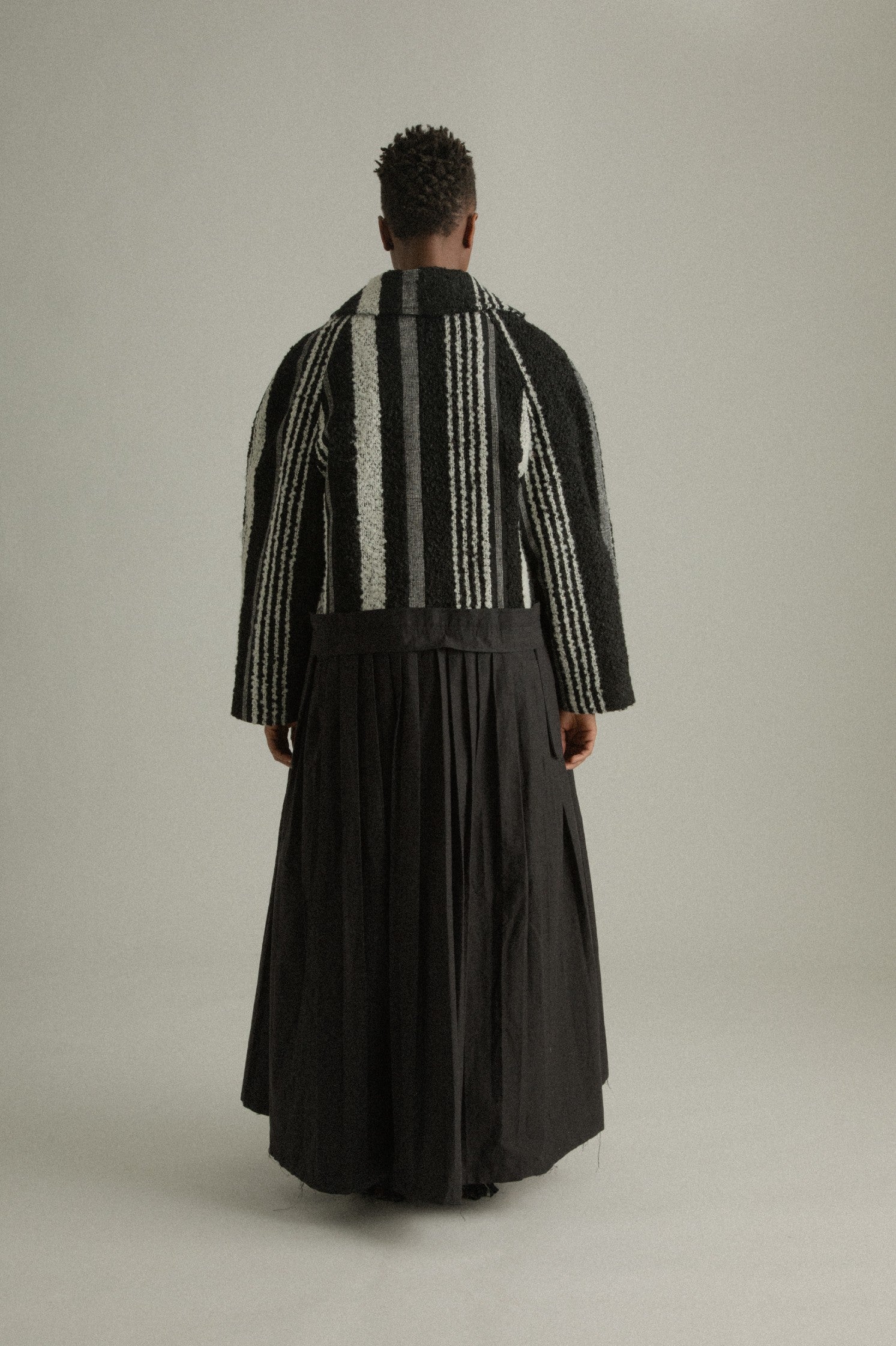 A back view of the Nino Coat highlighting the clean lines, structured shoulders, and intricate handwoven texture.