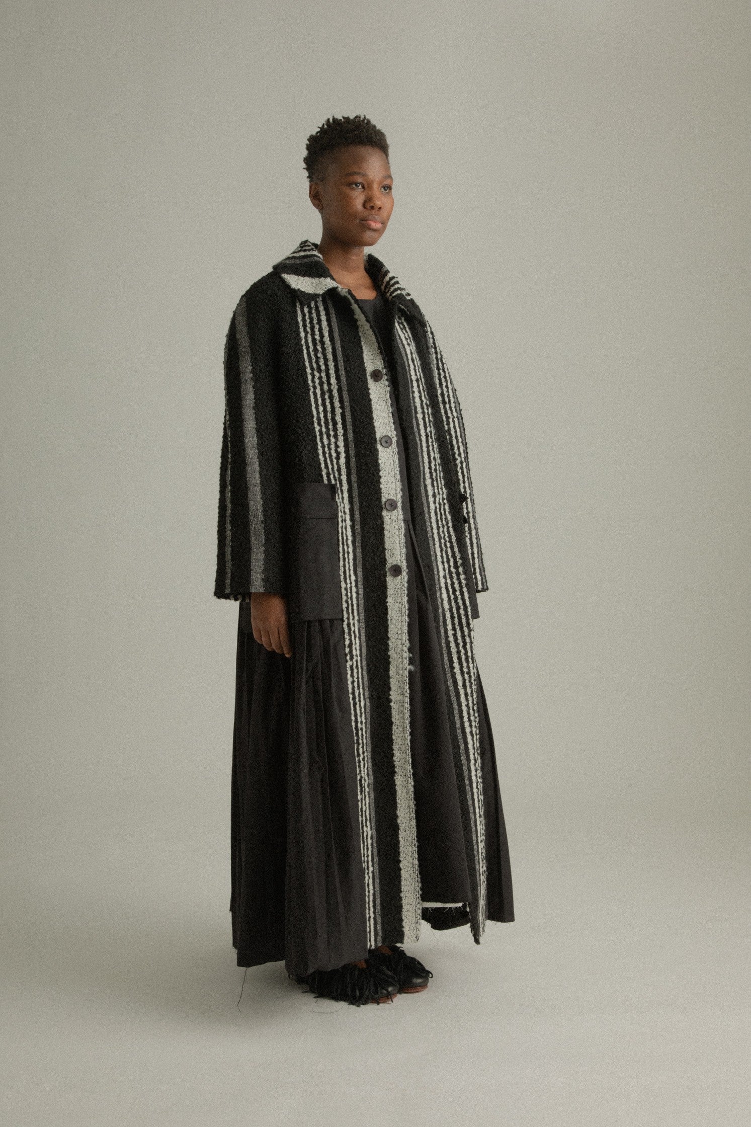 A side view of the Nino Coat revealing the flowing silhouette and subtle details of its dense mohair-cotton blend fabric.