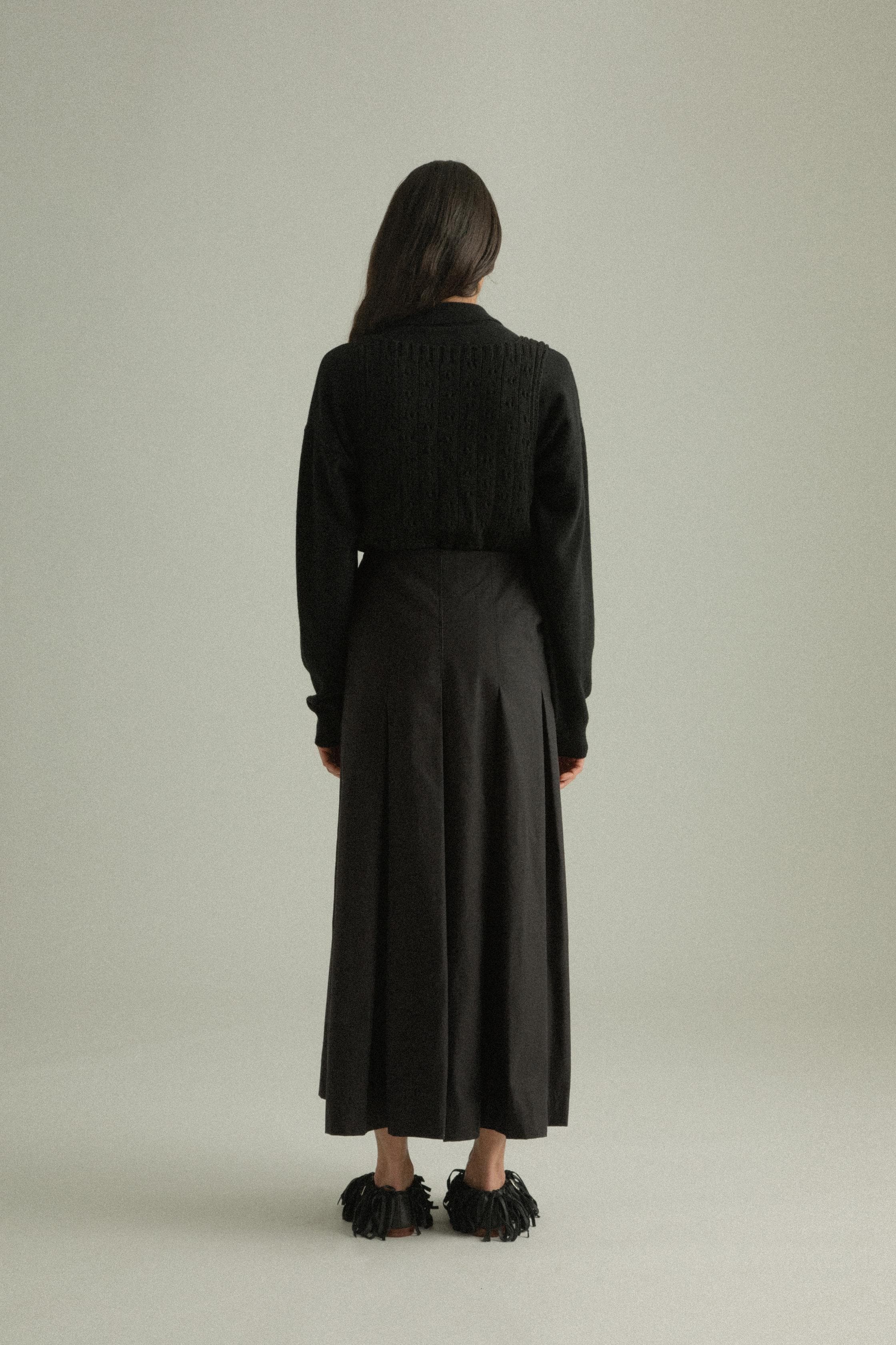 A model wearing the Rayna Pants, made from 100% organic cotton with a full pleat design. The pants feature a double-layered fabric and hand-pressed pleats, offering a flowing silhouette. The model is shown in front, side, and back views.