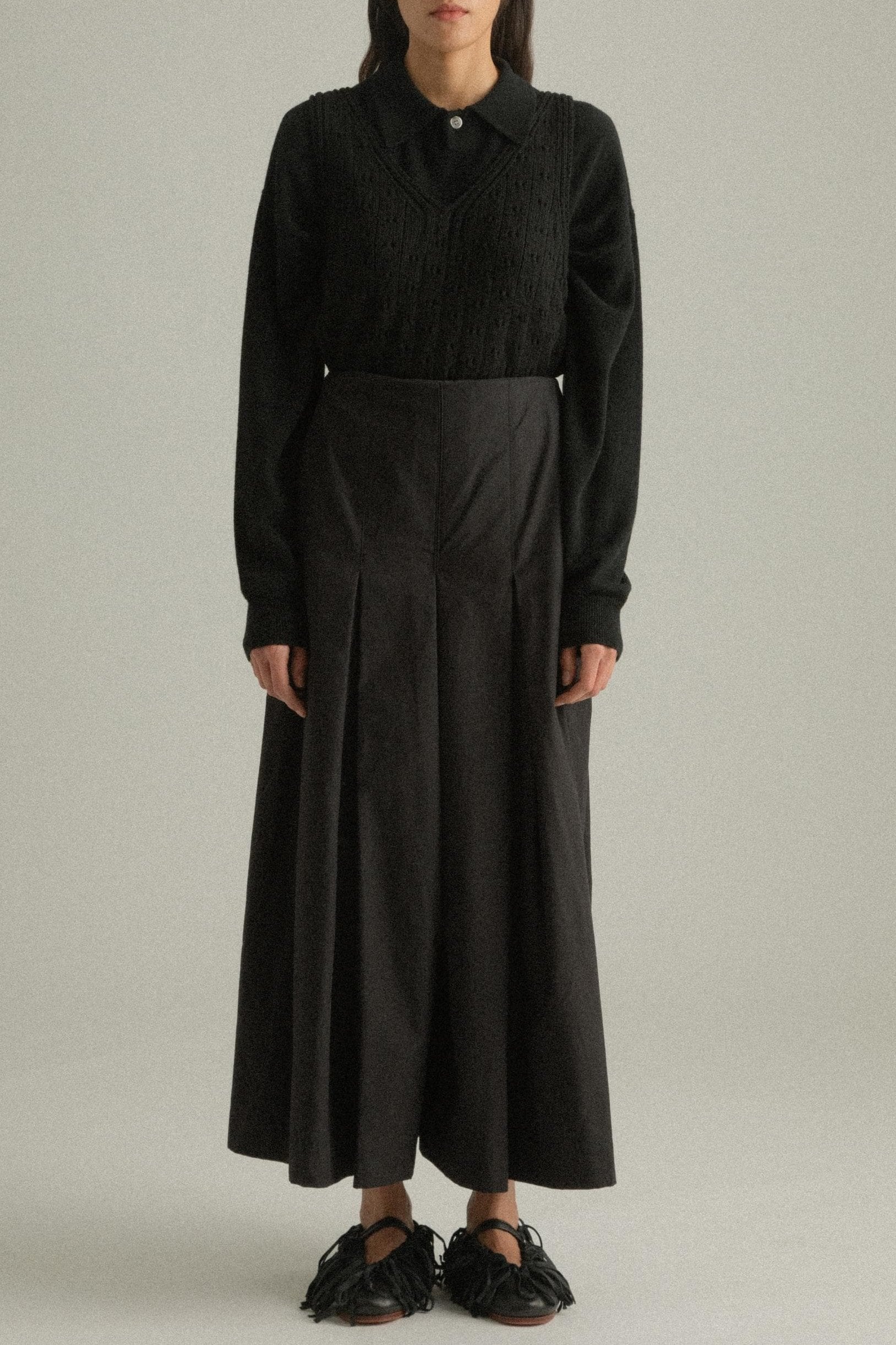 A model wearing the Rayna Pants, made from 100% organic cotton with a full pleat design. The pants feature a double-layered fabric and hand-pressed pleats, offering a flowing silhouette. The model is shown in front, side, and back views.