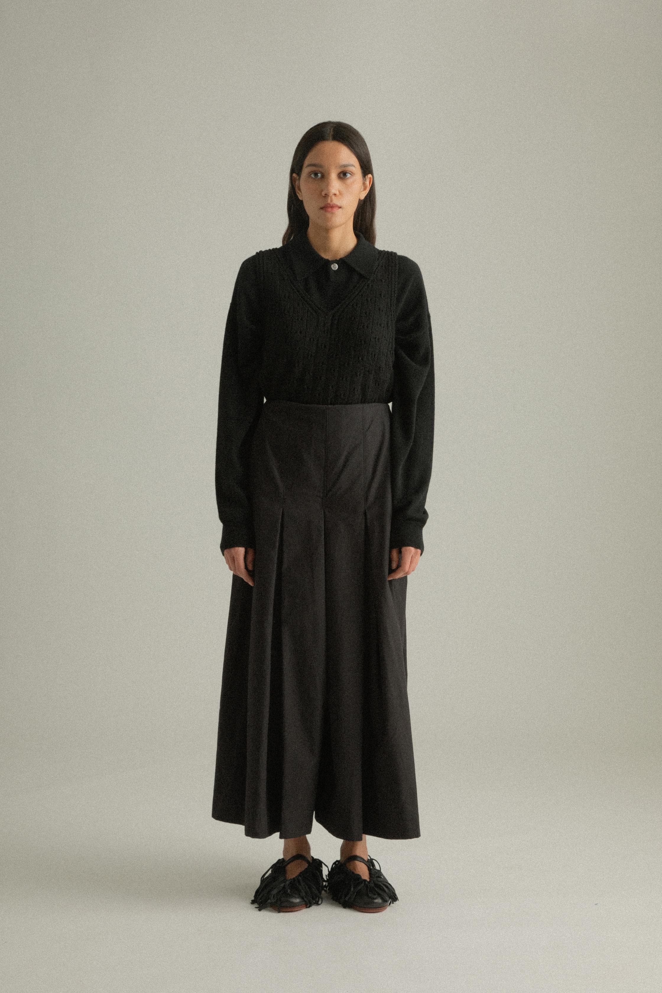 A model wearing the Rayna Pants, made from 100% organic cotton with a full pleat design. The pants feature a double-layered fabric and hand-pressed pleats, offering a flowing silhouette. The model is shown in front, side, and back views.