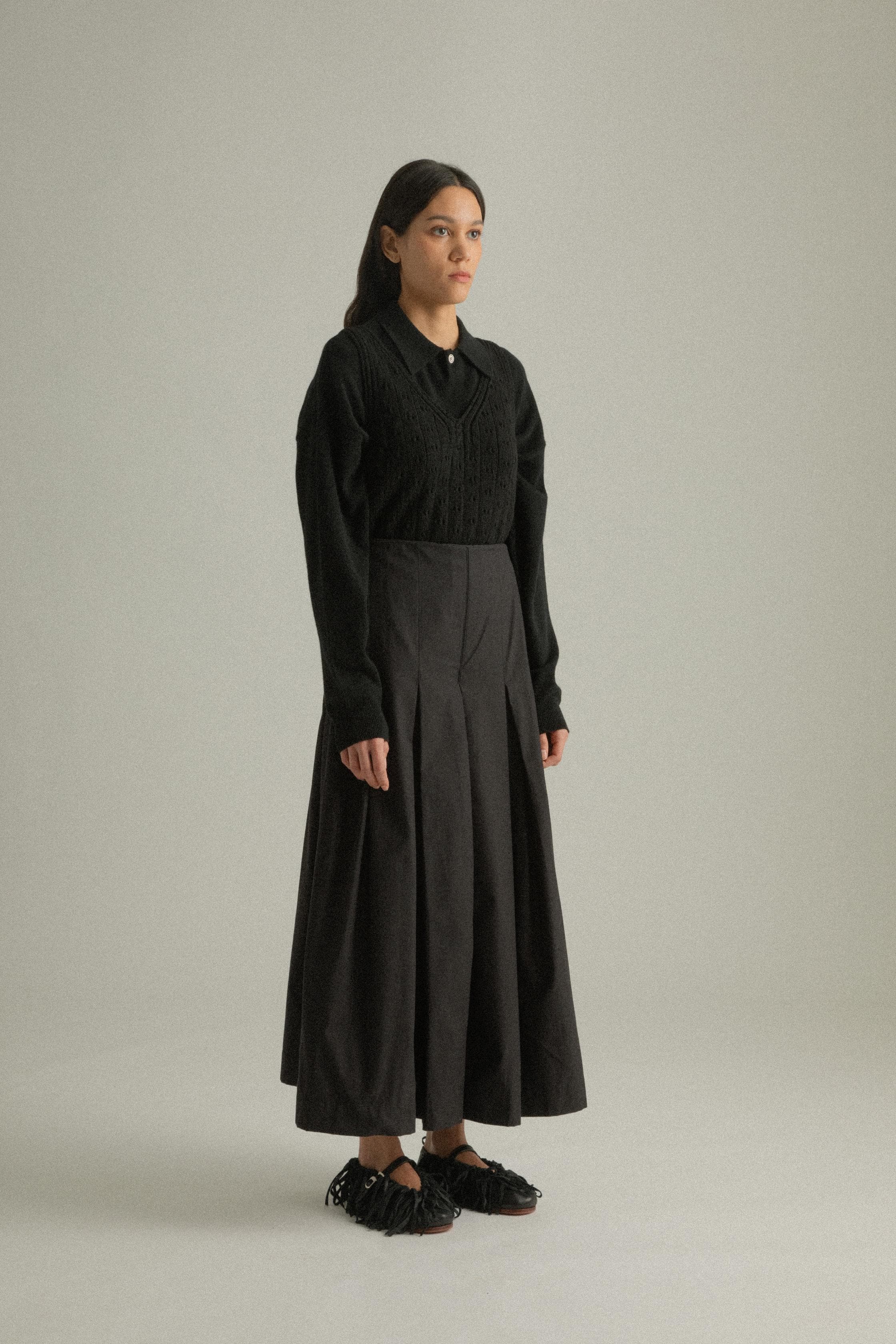 A model wearing the Rayna Pants, made from 100% organic cotton with a full pleat design. The pants feature a double-layered fabric and hand-pressed pleats, offering a flowing silhouette. The model is shown in front, side, and back views.