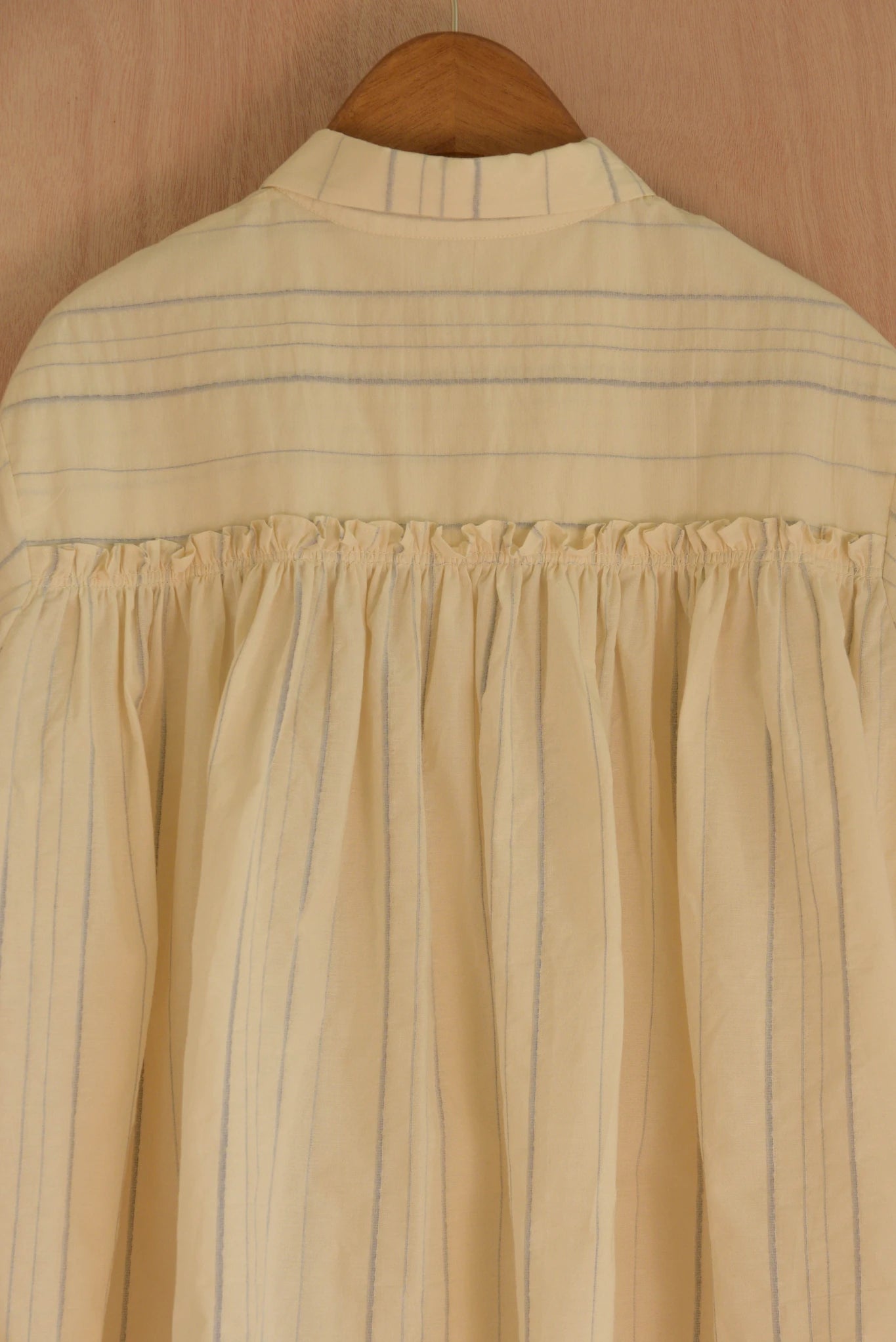 Beige shirt with blue stripes on a wooden hanger against a beige background